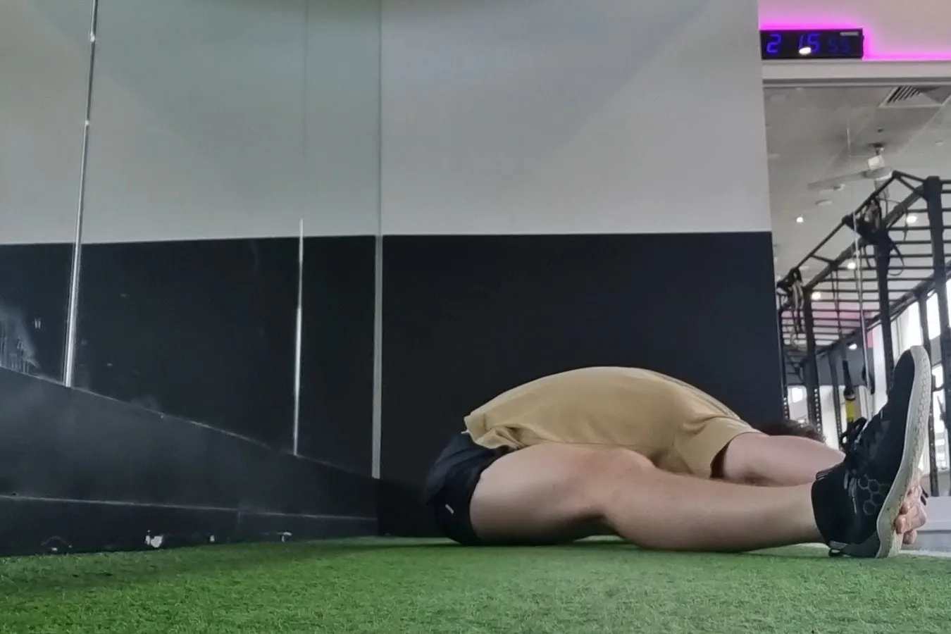 The same seated fold months later, on gym turf, his chest and head now resting flat along his legs with his hands at his feet