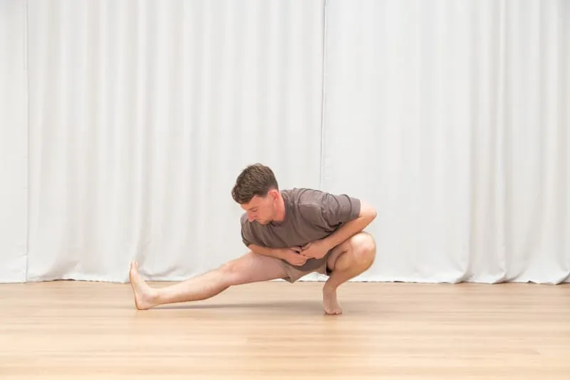 Keegan in a deep one-legged squat with the opposite leg extended straight along the floor, torso upright and hands together in front of his chest