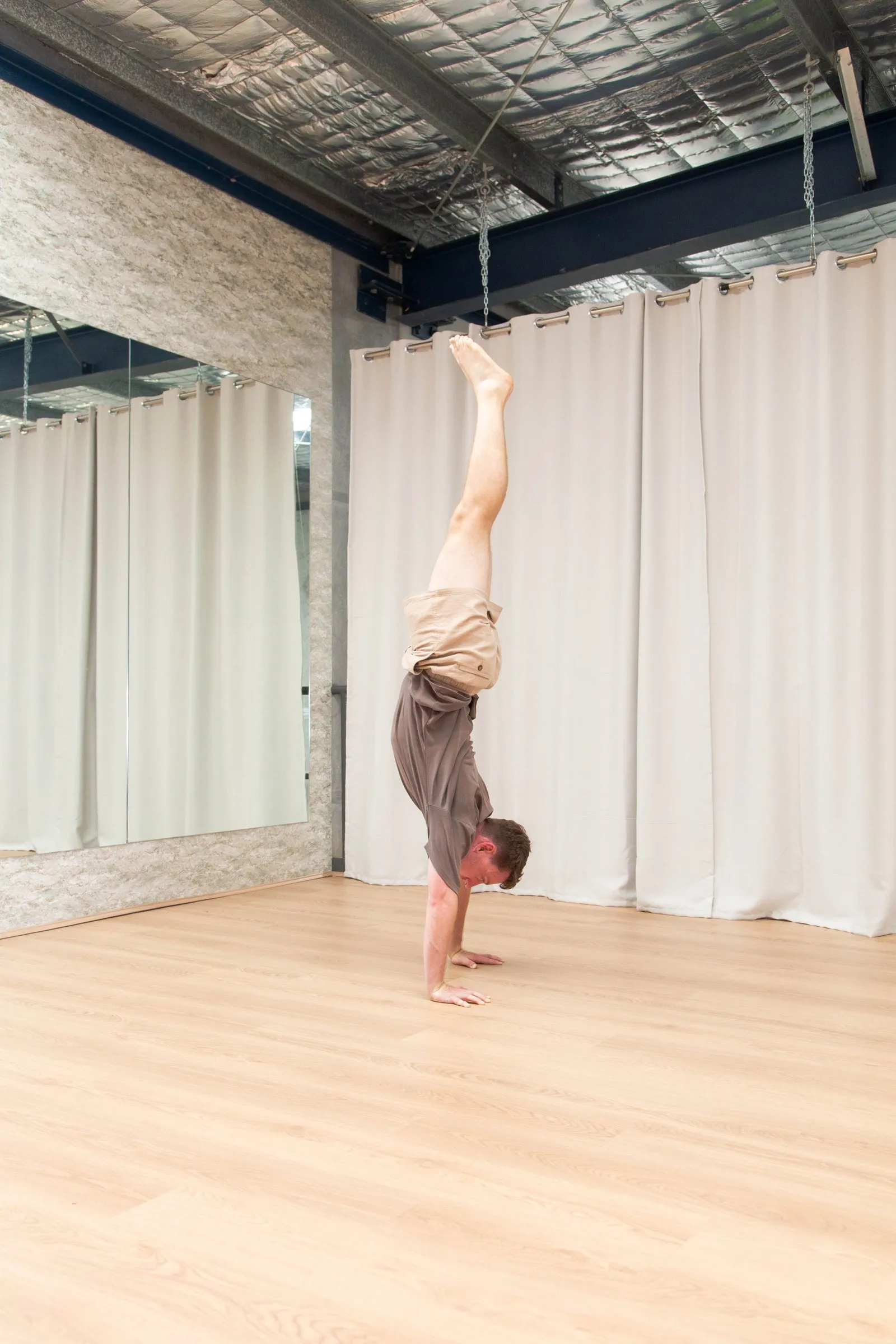 Keegan holding a straight handstand in a mirrored studio, legs together and fully extended