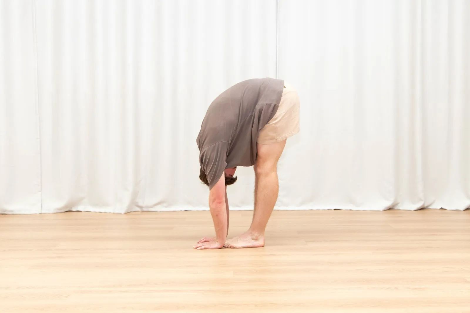 Keegan in a standing forward fold with straight legs, his palms flat on the floor in front of his feet