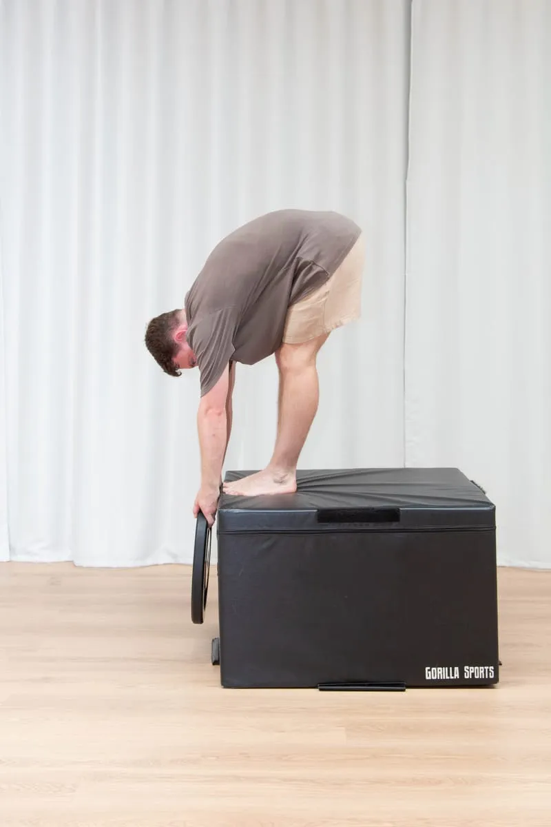 Keegan standing with his feet together, folded forward with both hands resting on top of a padded gym box