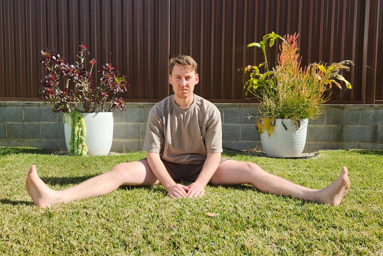 The same straddle seen from the front, showing how wide the legs are open, with his torso upright and his hands resting in his lap.