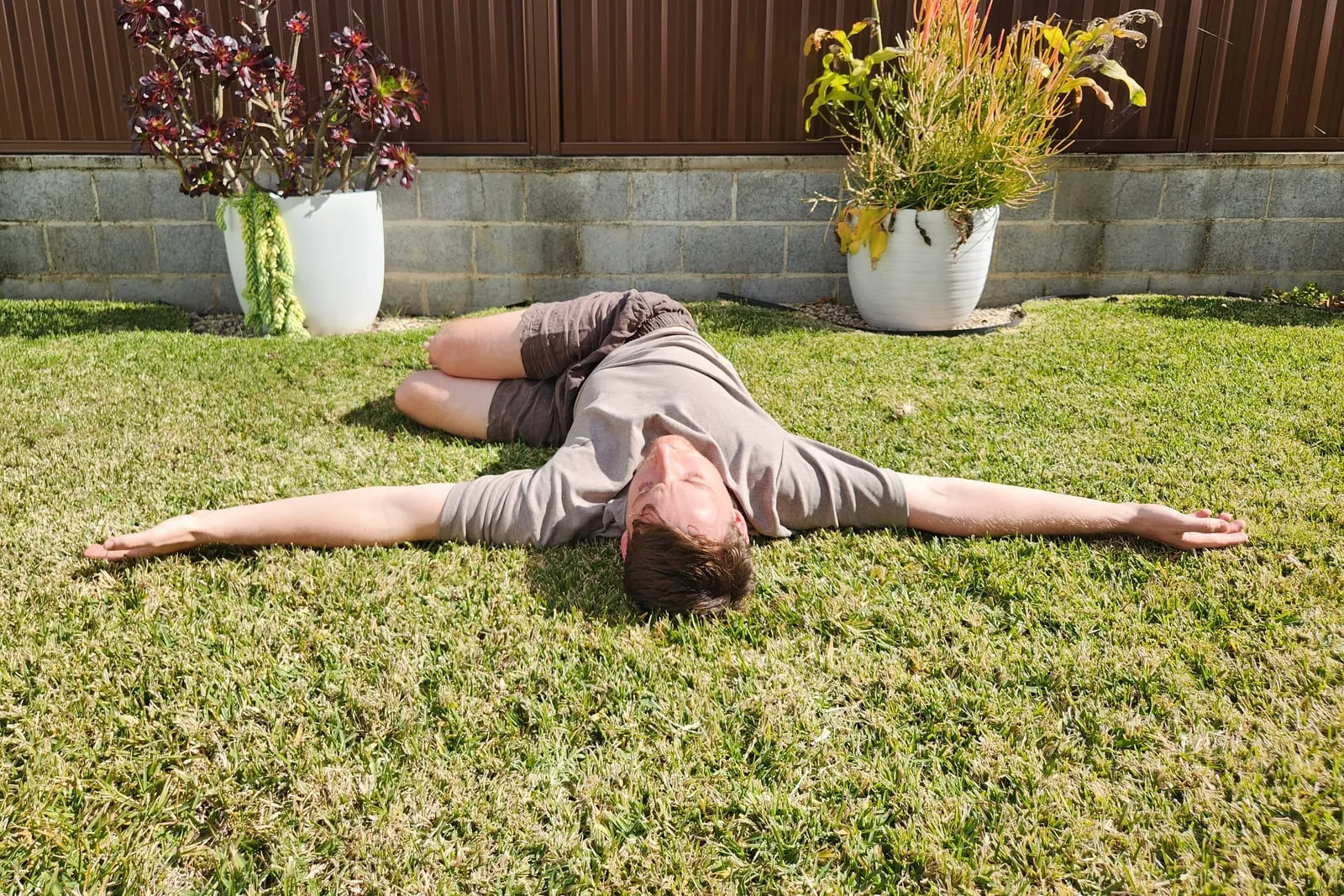 Keegan lying on his side on grass with his knees stacked and bent, sweeping his top arm across his body so that shoulder reaches the ground behind him.