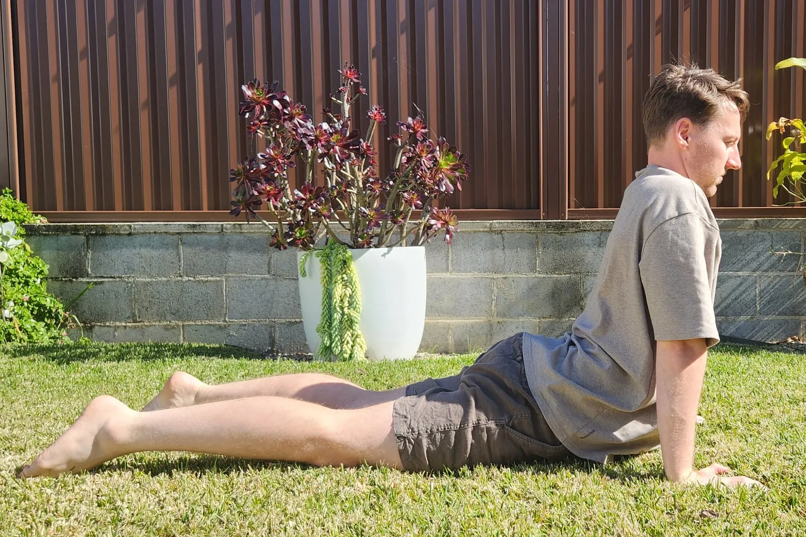Keegan in a cobra on grass, seen from the side, arms straight with his shoulders over his hands, chest lifted and his hips still resting on the ground.